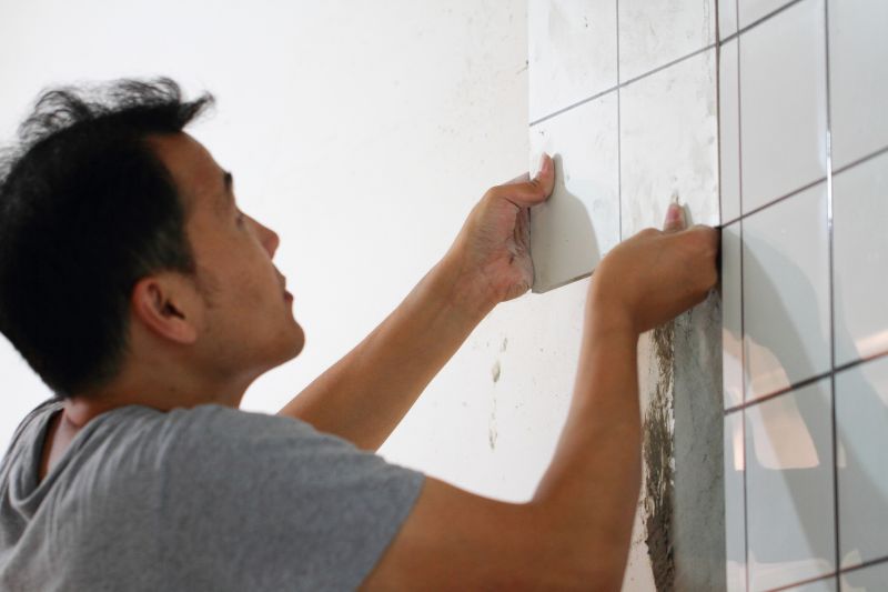 Installer laying ceramic tiles on bathroom floor.